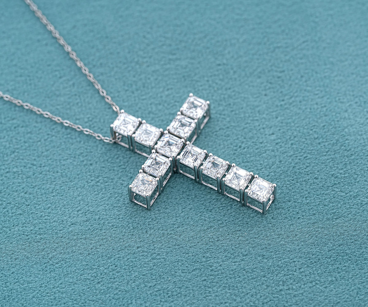 A silver cross pendant necklace set with clear rectangular gemstones, resting on a textured teal surface.