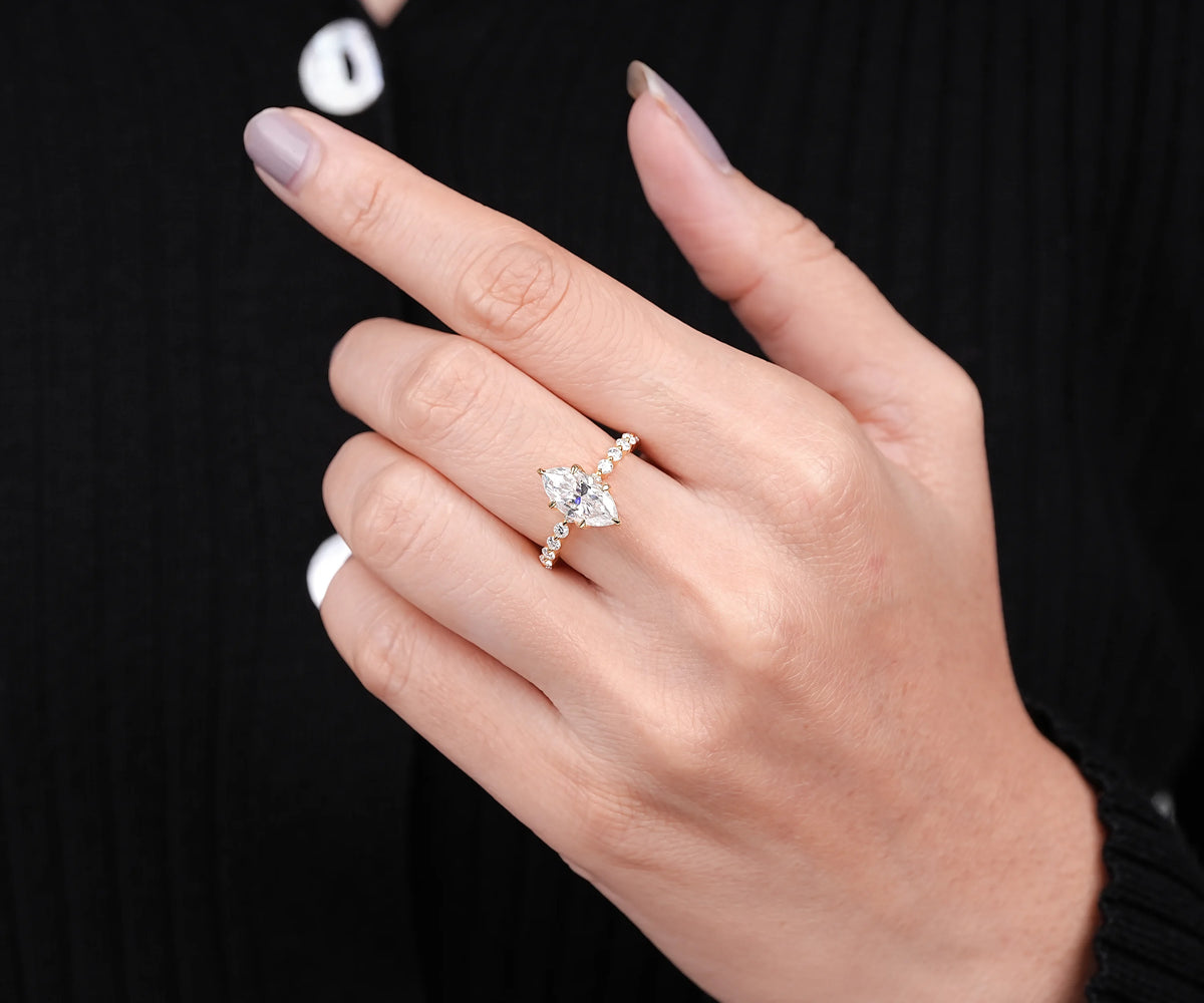A close-up of a hand wearing a silver-toned ring with a marquise-cut center stone and small side stones, set against a black ribbed sweater background.