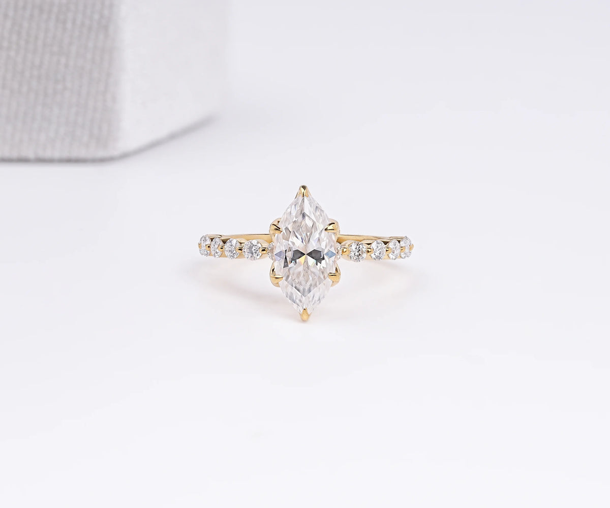 A yellow gold ring featuring a marquise-cut clear center stone and a pavé band with small round stones, photographed on a clean white background.