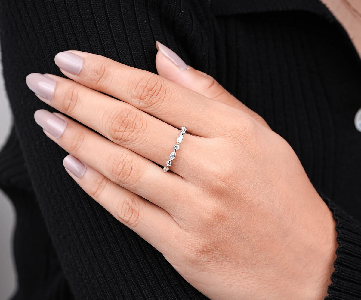 A close-up of a person's hand wearing a delicate silver band ring with small clear stones, set against a black ribbed sweater.