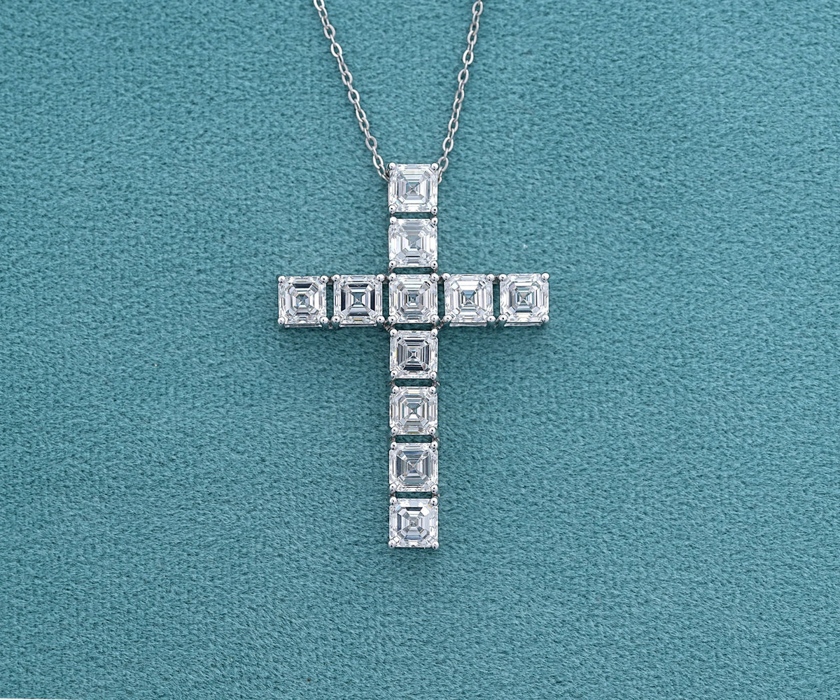 A silver cross pendant necklace adorned with square-cut clear gemstones, displayed on a textured teal background.