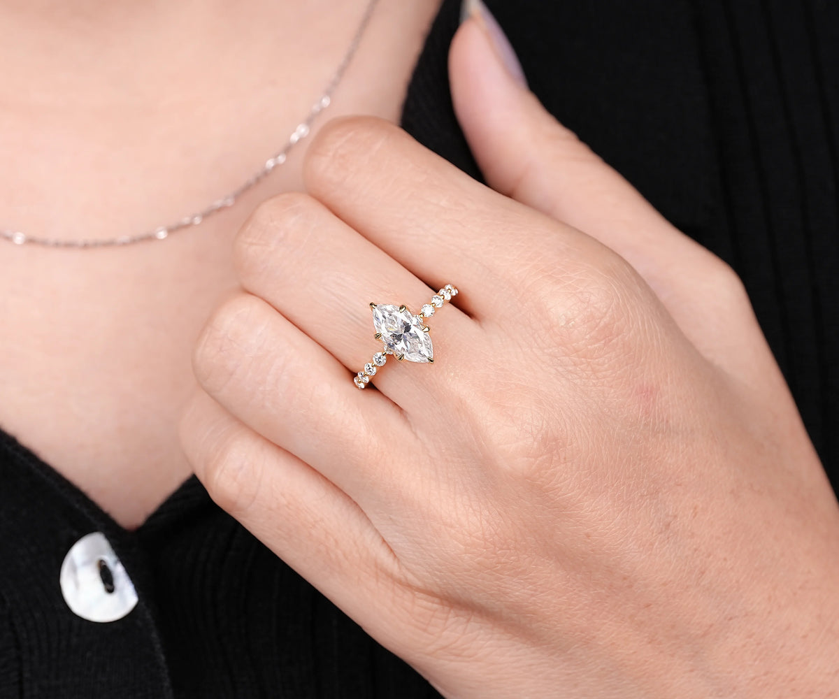 A close-up of a person's hand wearing a silver-toned ring with a marquise-cut clear gemstone and small side stones, against a black top background.