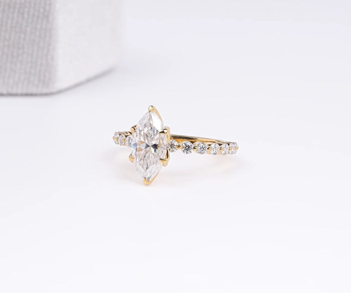 A yellow gold ring featuring a marquise-cut clear center stone and a pavé band with small round stones, photographed on a clean white background.